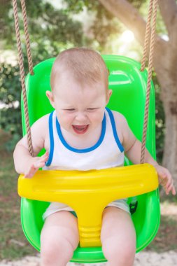 Küçük çocuk komik bir ifadeyle salıncakta oturuyor. Çocuk çığlık atıyor ya da gülüyor. Yaz güneşli bir gün, dinlenme, dikey fotoğraf, yakın çekim, portre