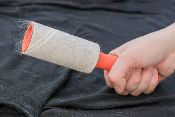 Velcro roller met oranje handvat voor het verzamelen van wol, haar, stof in een persoon hand tegen een achtergrond van zwart materiaal. dierenhaar zit vast op de roller. Thuis kleren schoonmaken. Close-up — Stockfoto