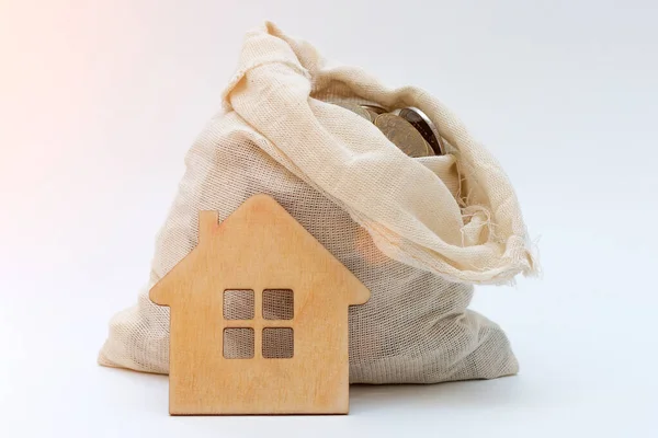 Open money bag with a model of a wooden house on a white background. Idea - Selling a house. Apartment purchase. Real estate market. Rent of housing by the day. Housing prices, credit, debt. — ストック写真