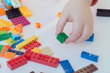 Çocuk eli, tasarımcının, yapı taşının küpünü alır. Yukarıdan görünüm, yakın plan, yatay fotoğraf