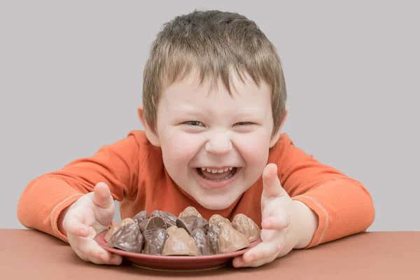 Een Vrolijk Lachend Kind Met Een Bord Chocolaatjes Jongen Zit — Stockfoto