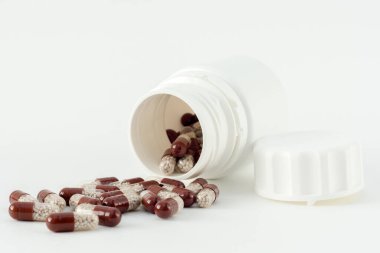 Kahverengi haplar beyaz bir şişeden dökülür. İçinde granüller olan kapsüller. İlaçlar, vitaminler, antibiyotikler. beyaz arkaplan, yatay fotoğraf