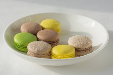 Beyaz bir tabakta renkli kurabiyeler. Nefis Fransız lezzeti. yatay fotoğraf. Yakın çekim, üst görüş. yeşil, sarı, kahverengi kurabiyeler. Elma, çikolata ve limon tadı