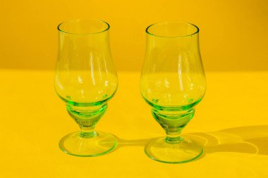 Sarı arka planda iki boş yeşil cam kadehler. Yatay fotoğraf, yakın plan..