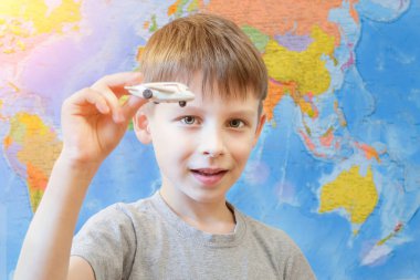 Dünya haritasının arka planında elinde oyuncak bir uçakla anaokulu çocuğu. Çocuk kameraya bakıyor. Konsept - seyahat hayalleri, yaz tatili, çocuk oynuyor. Yatay fotoğraf