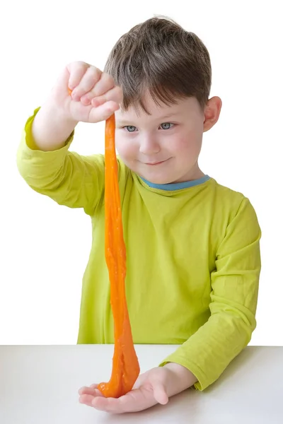 De jongen speelt met oranje slijm. Kijk, glimlacht als het stroomt. Het concept is de ontwikkeling van creatief denken en fijne motoriek, het behoud van de toon van de handen, het verlichten van stress. Verticaal — Stockfoto