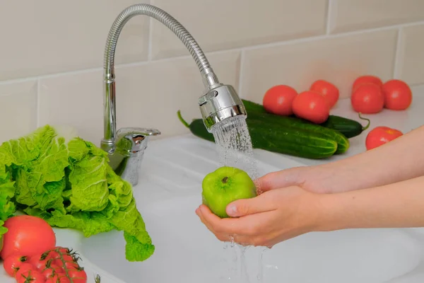 Kadın elleri mutfakta muslukla sebzeleri yıkıyor. Yakın plan, yatay fotoğraf. Kavram - sağlıklı yiyecekler, vitaminler, vejetaryenlik, yemek pişirme.