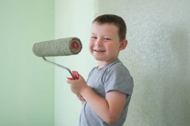 Elinde boya silindiri olan bir çocuğun portresi. Mutlu çocuk duvarları boyuyordu. yatay fotoğraf. Çerçeveye bakıyor. İçinin yeşil renklerle yenilenmesi