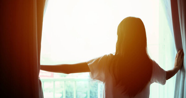 Asian women  wake up in her bed fully rested and open the curtains in the morning to get fresh air on sunshine 