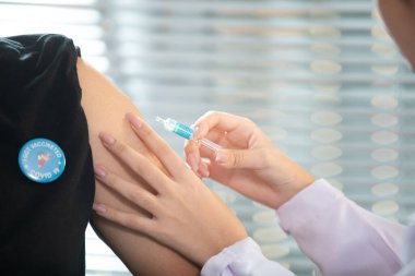 Doktor elinde şırıngayla Covid-19 ya da Coronavirus aşısı olan hastaya enjeksiyon yapacak. Doktor da Covid-19 aşısını yaptırdığını doğruladığı için adama etiket yapıştırıp iğneler takacak.