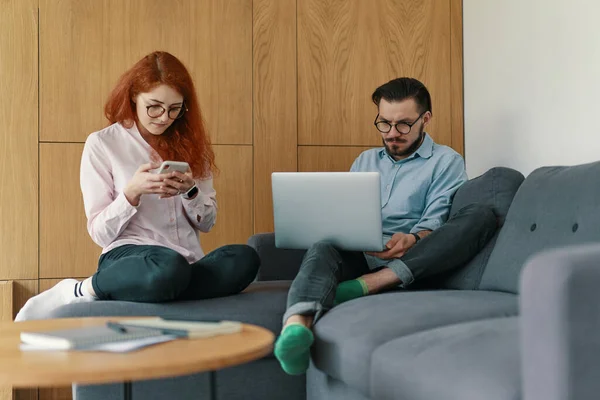 Jonge familie freelancers werken vanuit huis. Een jongen en een meisje in casual kleding met gadgets — Stockfoto