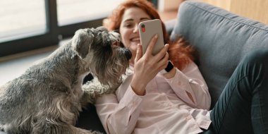 Kanepede köpeğiyle oturan ve akıllı telefon kullanan bir kız.