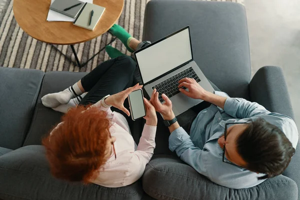 Top weergave van het gezin paar rusten op comfortabele bank met plezier met behulp van laptop en telefoon — Stockfoto