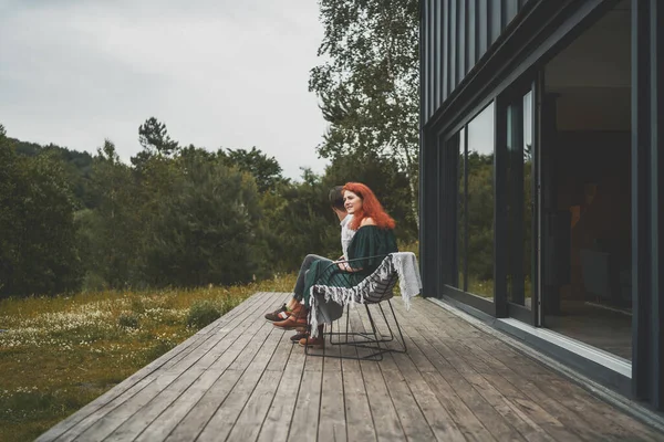 Vista laterale della coppia di famiglia che trascorre del tempo insieme sul portico in legno della casa di campagna — Foto Stock