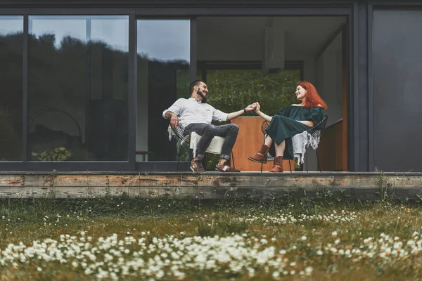 Молода подружня пара сидить на терасі сучасного будинку в горах . — стокове фото