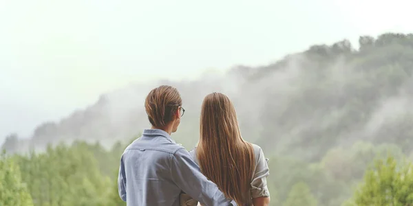 Visão traseira do jovem casal desfrutando de bela vista sobre a floresta nas montanhas — Fotografia de Stock