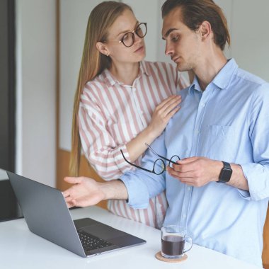 Genç bir çift dizüstü bilgisayarlarıyla mutfakta duruyor ve evden çalışıyor.