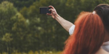 Genç çiftlerin arka planda eğlenmeleri ve telefonda doğanın fotoğraflarını çekmeleri.