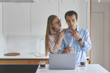 Genç bir çiftin dizüstü bilgisayarlarıyla mutfakta durup evden çalışmalarını ön plana çıkarıyorum.