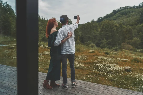 Vista trasera de la joven pareja familiar haciendo selfie en el teléfono inteligente en la terraza — Foto de Stock