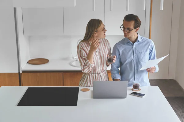 Jong stel staat op de moderne keuken met laptop en smartphone tijdens het werken vanuit huis — Stockfoto