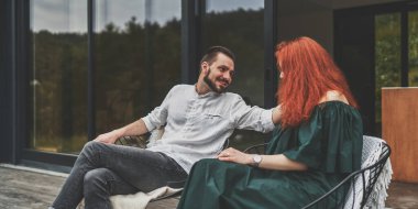 Modern evin terasında oturan mutlu çift dışarıda güzel manzaranın tadını çıkarıyor.