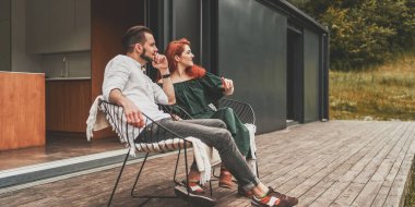 Genç çift modern evin terasında oturuyor ve güzel manzaranın tadını çıkarıyor.