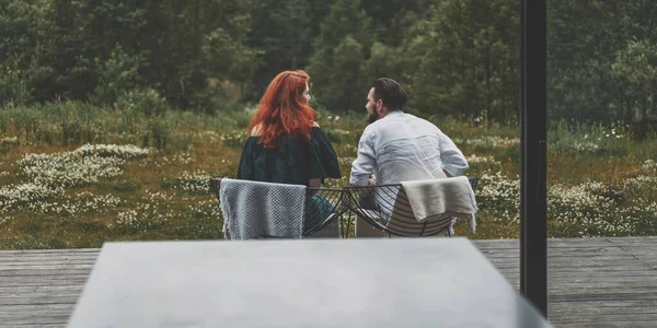 Back view of young couple sitting on the terrace of modern house, enjoying beautiful view outdoors