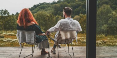 Terasta oturan ve dağlara bakan çiftin arka manzarası.