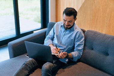 Genç işadamı evde dizüstü bilgisayarla çalışıyor.