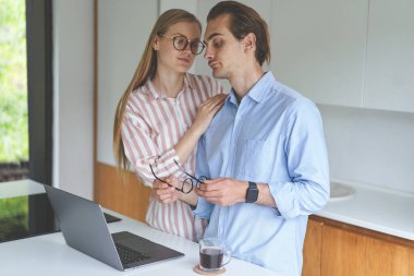 Genç bir çift dizüstü bilgisayarlarıyla mutfakta duruyor ve evden çalışıyor.