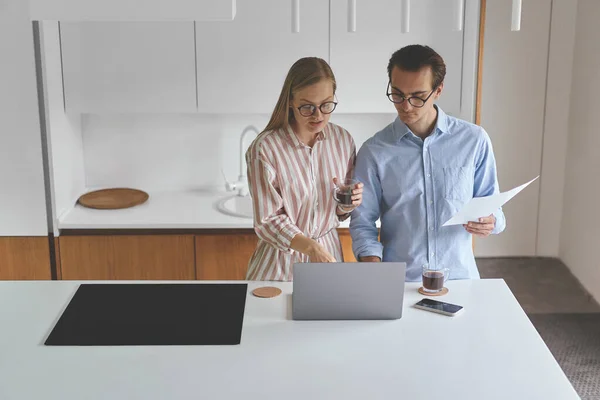 Jong stel freelancers staat op de moderne keuken met laptop en smartphone — Stockfoto