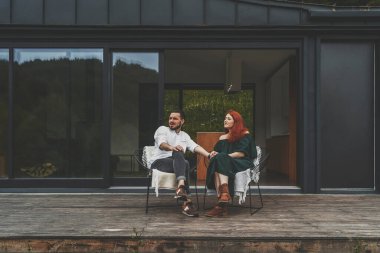 Büyük kır evinin terasında oturan mutlu bir aile.