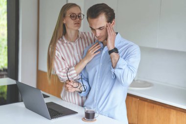 Genç bir çift dizüstü bilgisayarlarıyla mutfakta duruyor ve evden çalışıyor.