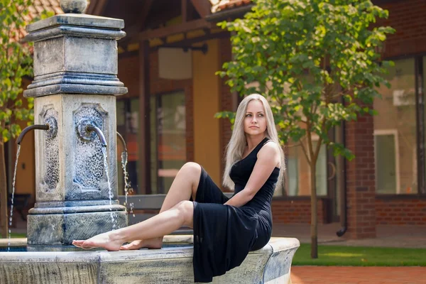 Woman sitting on the old drinking fountain barefoot — Stock Photo, Image