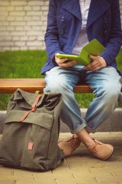 Tablet ve sırt çantası ile bankta oturan öğrenci kız