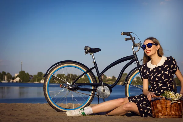 Hermosa joven en la playa con bicicleta y flores en la cesta —  Fotos de Stock