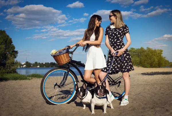 Dwie piękne dziewczyny na plaży z roweru i buldogi francuskie — Zdjęcie stockowe