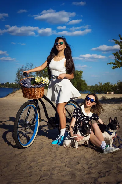 Dvě krásné dívky na pláži s kola a francouzský buldok — Stock fotografie