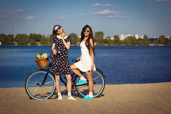 Twee mooie meisjes op het strand met fiets en bloemen in mand — Stockfoto