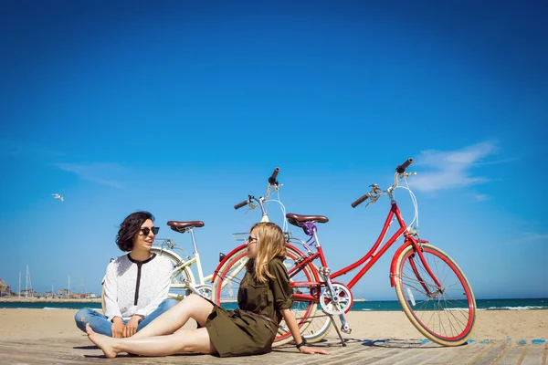 Twee vrienden zittend op het strand met fietsen — Stockfoto