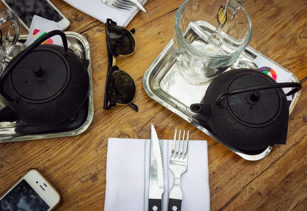 Vista superior da mesa de jantar com dois bules, copos, telefone e óculos de sol — Fotografia de Stock