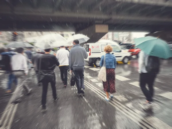 Motion blurred pedestrians crossing street on rainy day Stock Picture