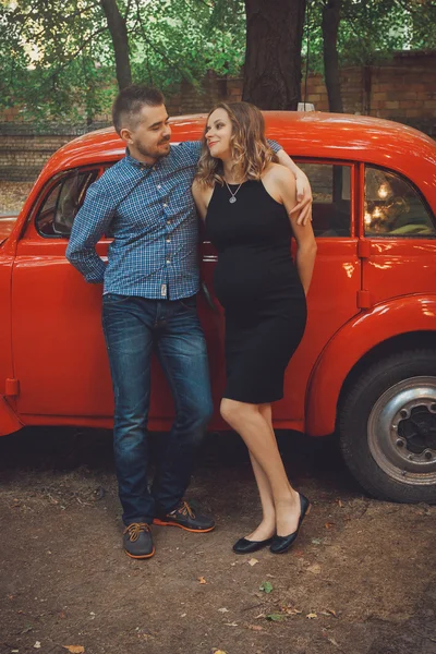 Hombre y mujer embarazada cerca de coche rojo — Foto de Stock