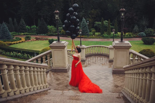 Preciosa mujer en vestido rojo con globos negros — Foto de Stock