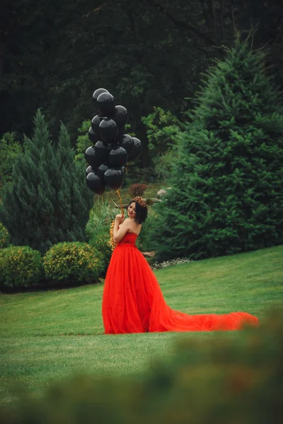 Hinreißende Frau im roten Kleid mit schwarzen Luftballons — Stockfoto