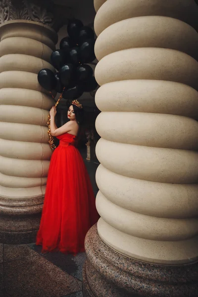 Preciosa mujer en vestido rojo con globos negros — Foto de Stock