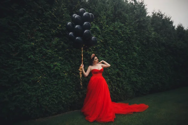 Hinreißende Frau im roten Kleid mit schwarzen Luftballons — Stockfoto