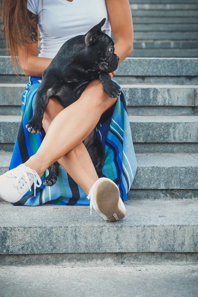 Kadın bacaklarının arasına merdivenlerde oturan siyah Fransız bulldog köpek yavrusu — Stok fotoğraf
