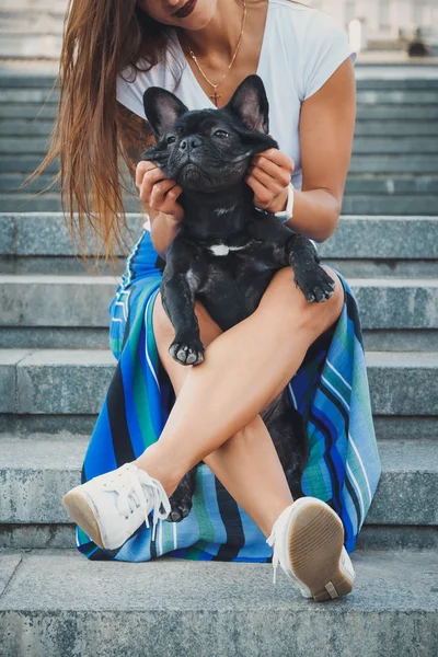 Negro bulldog francés cachorro sentado en las escaleras entre las piernas femeninas — Foto de Stock